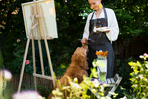 Canvas Print Young female artist working on her art canvas painting outdoors in her garden with golden retriever keeping her company
