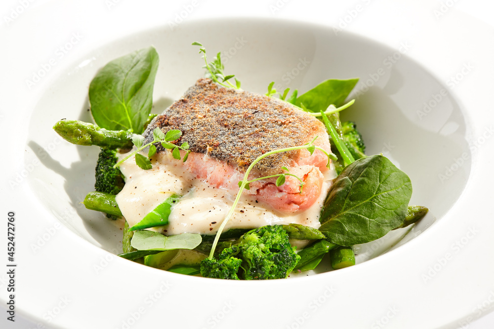 Panfried Fish with broccoli and green spinach. Healthy roasted cod with asparagus espuma. Fried Fish on white restaurant plate isolated on white background. Panfried Fish with broccoli and green spinach. Healthy roasted cod with asparagus espuma. Fried Fish on white restaurant plate isolated on white background.