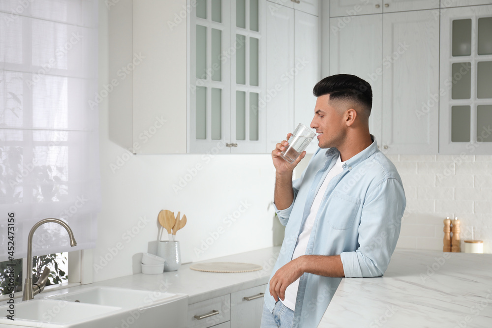 Man drinking tap water from glass in kitchen Man drinking tap water from glass in kitchen