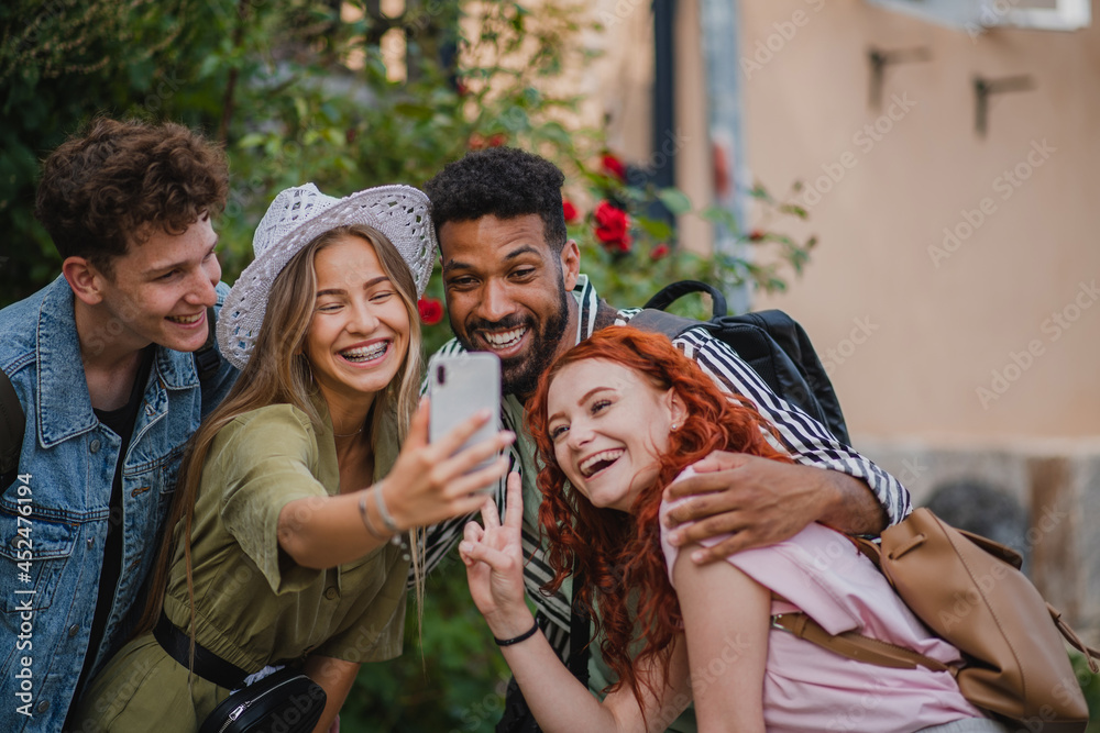 Obraz premium Portrait of group of young people outdoors on trip in town, taking selfie with smartphone.