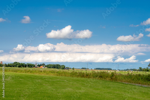Summer countryside landscape  Flat and low land with green meadow under blue sky  Typical Dutch polder with canal or ditch on the field  Small villages in Groningen  A city in the northern Netherlands