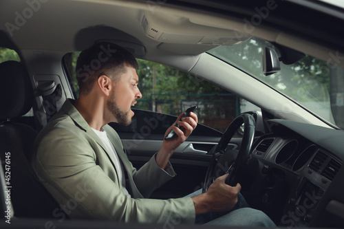 Stressed businessman talking on phone in driver's seat of modern car