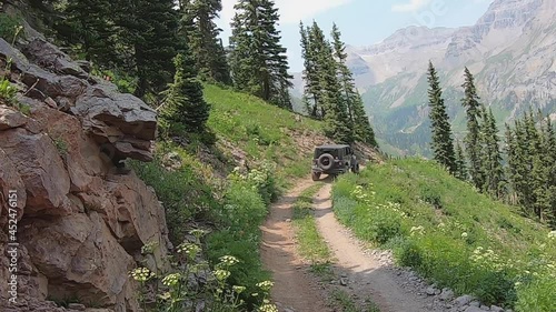 POV following a Jeep on Sidney Trail cut into a steep alpine meadow side high above Yankee Boy Basin of the San Juan Mountains in Colorado; concepts of adventure, exploration and mountain landscape photo