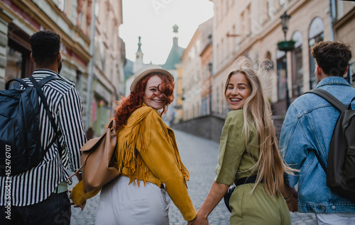 Rear view of group of happy young people outdoors on trip in town, walking and looking back. © Halfpoint