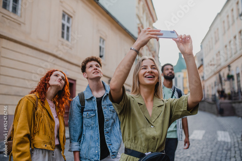 Group of young people sightseeing outdoors on trip in town, taking photographs with smartphone.