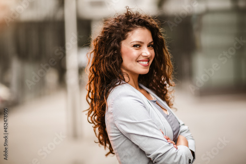 Caucasian businesswoman with curly hair posing outside