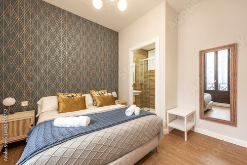King bed with beautiful gold cushions, full-length mirror and bathroom with shower in the back in a vacation rental apartment