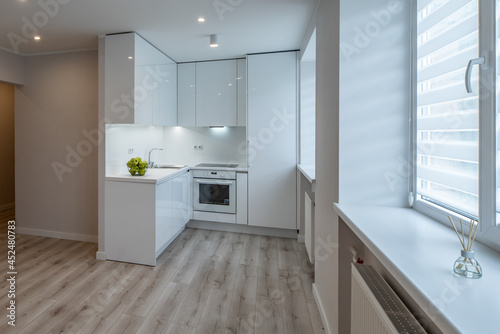 Bright interior of contemporary renovated apartment. White kitchen with fridge and oven. Parquet floor.