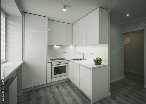 Bright interior of contemporary renovated apartment. White kitchen with fridge and oven. Parquet floor.