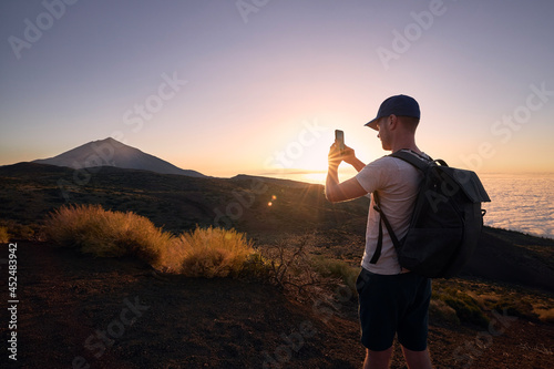 Man photograps by mobile phone against landscape at beautiful sunset. Volcano Pico de Teide in Canary Islands, Spain. © Chalabala