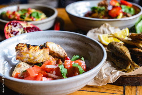 A dinner of fish and tomato salad served in a bowl on the table with other dishes.