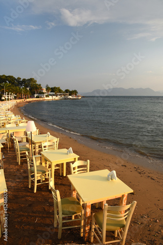 tables set for dinner on the beach at sunset over the sea in Aegina in Greece © sergioboccardo