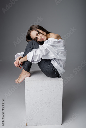 A girl in a white shirt and trousers is sitting on a cube