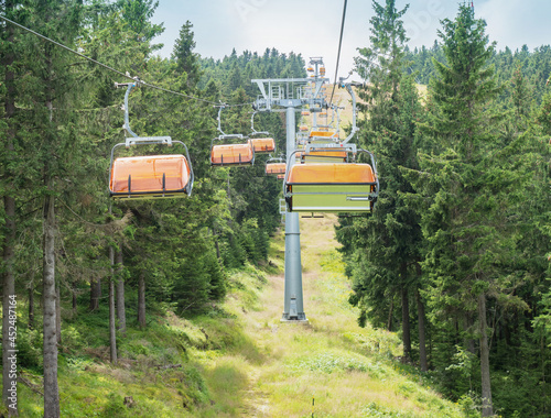 Foto Chairlift with orange wind cover of seats shaking on the up way through forest