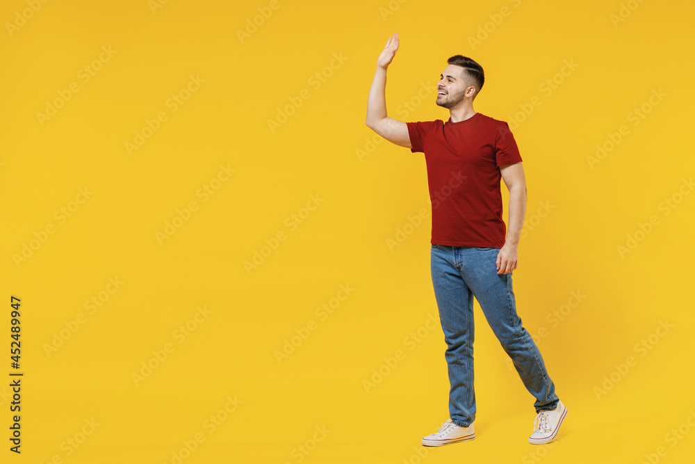 Full length smiling happy caucasian young man 20s wear red t-shirt casual clothes walking going look camera isolated on plain yellow color wall background studio portrait. People lifestyle concept Full length smiling happy caucasian young man 20s wear red t-shirt casual clothes walking going look camera isolated on plain yellow color wall background studio portrait. People lifestyle concept