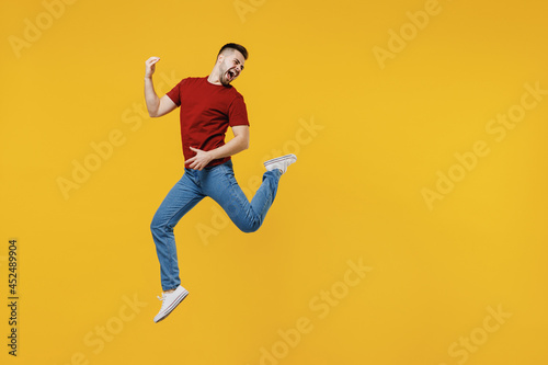 Full length overjoyed expressive fun happy young man wear red t-shirt casual clothes jump high playing guitar isolated on plain yellow color wall background studio portrait. People lifestyle concept. © ViDi Studio