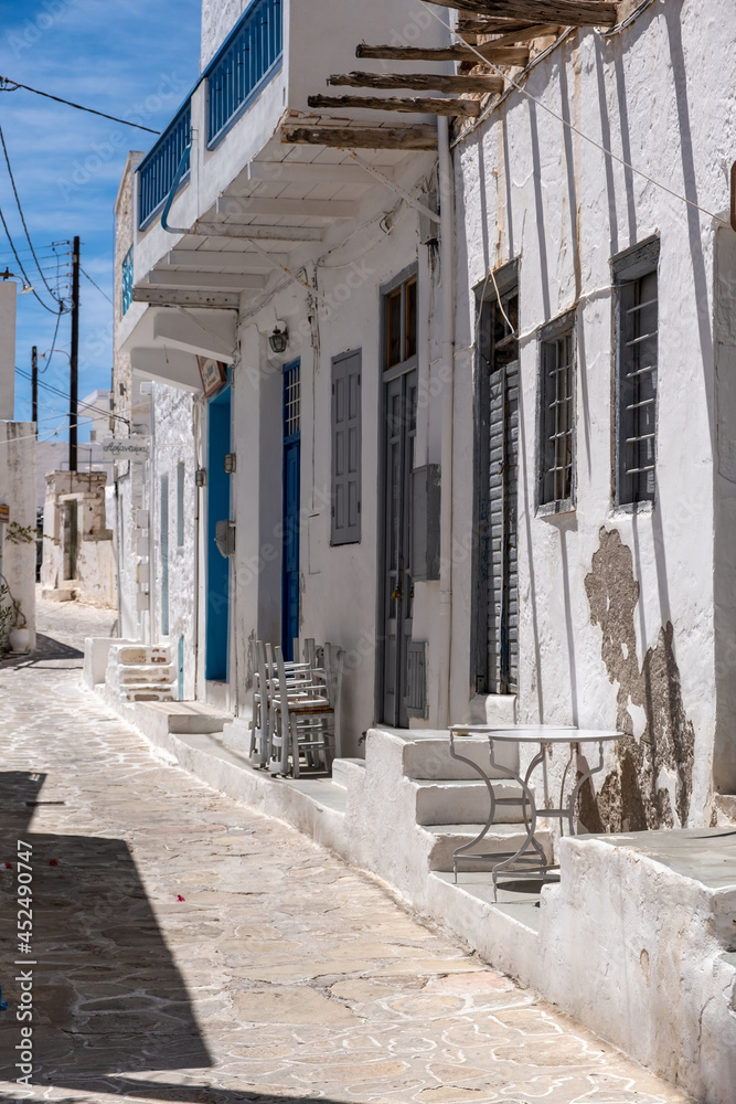 Whitewashed closed shops cobblestone alley Kimolos island Cyclades Greece. Vertical
