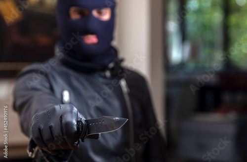 Burglar with balaclava, holding a knife in gloved hand,