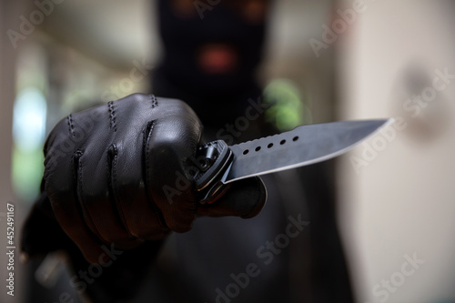 Fényképezés Burglar with balaclava, holding a knife in gloved hand,