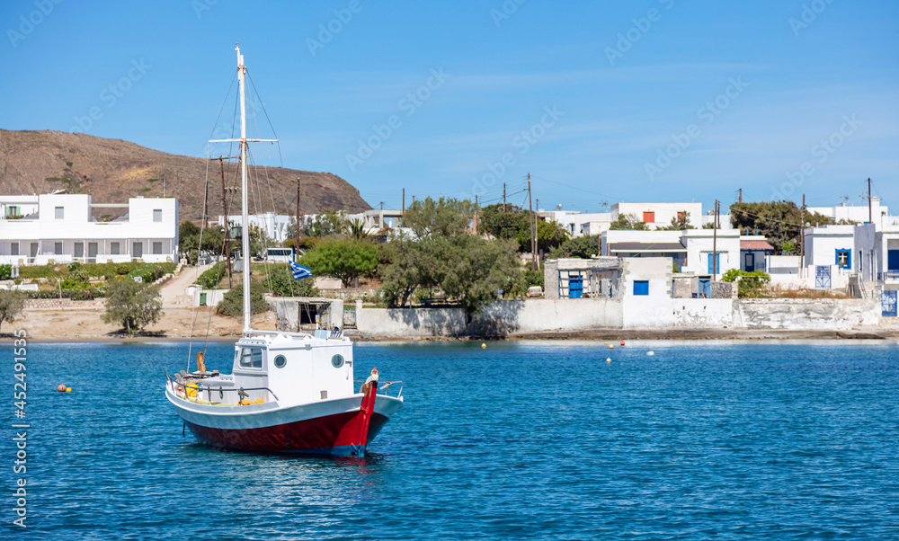 Milos island Cyclades Greece. Whitewashed buildings at seaside  fishing boat moored in calm blue sea