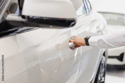 Close up man male hand arm customer buyer client in white shirt chooses auto want to buy new automobile open car door handle in showroom vehicle salon dealership store motor show indoor Sales concept