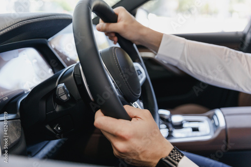 Close up cropped up photo shot hands arms european businessman man wearing white shirt sitting in BMW brand car salon driving hold steering wheel automobile modern vehicle. Car sales driver concept © ViDi Studio