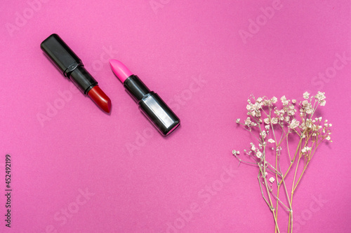 Fashion cosmetics photo of red and pink lipsticks and dry flowers on a pink background 