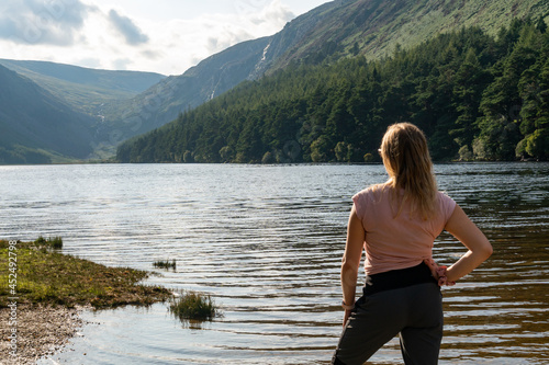 Girl resting on the lake shore at the Glendalough Valley. Panoramic idyllic view. County Wicklow Upper lake from miners way, Glenealo valley, Wicklow way, County Wicklow, Ireland.