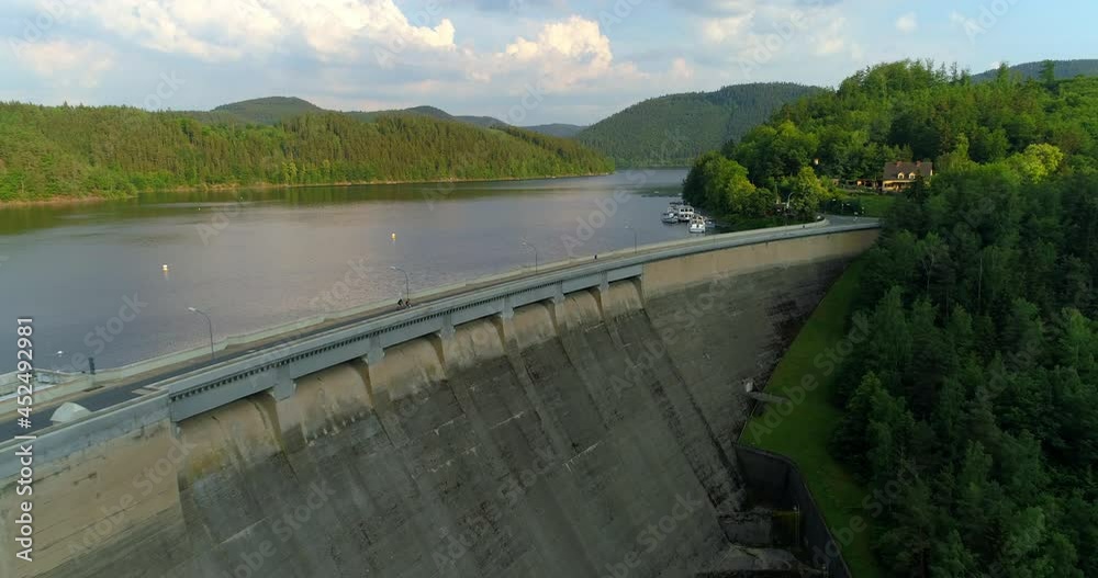 Aerial Forward Shot Of People Riding Bicycle On Dam Road, Drone Flying Over Lake In Forest On Sunny Day - Thuringia, Germany