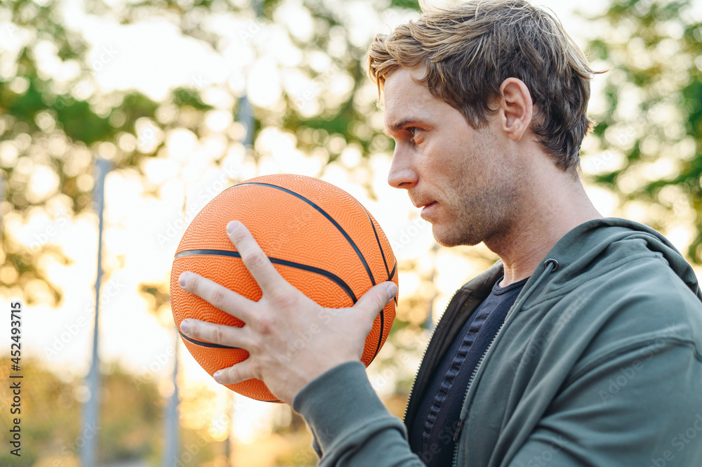 Side view young concentrated serious sunlit sporty sportsman man 20s wearing grey sports clothes training hold in hand ball play at basketball game playground court Outdoor courtyard sport concept