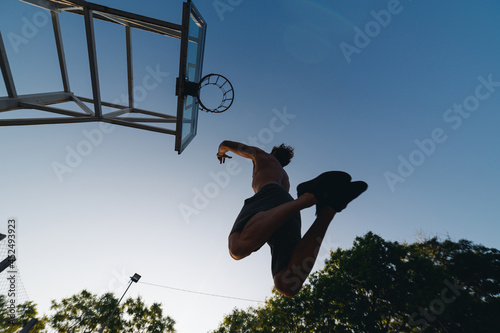 Bottom back view young strong sportsman man with naked torso shoot free throw jump scoring basket training ball at basketball game playground court on sky background Outdoor courtyard sports concept. © ViDi Studio