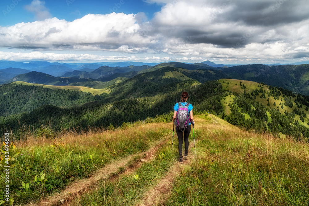 Obraz premium Woman hiker with backpack and trekking poles on hiking trail