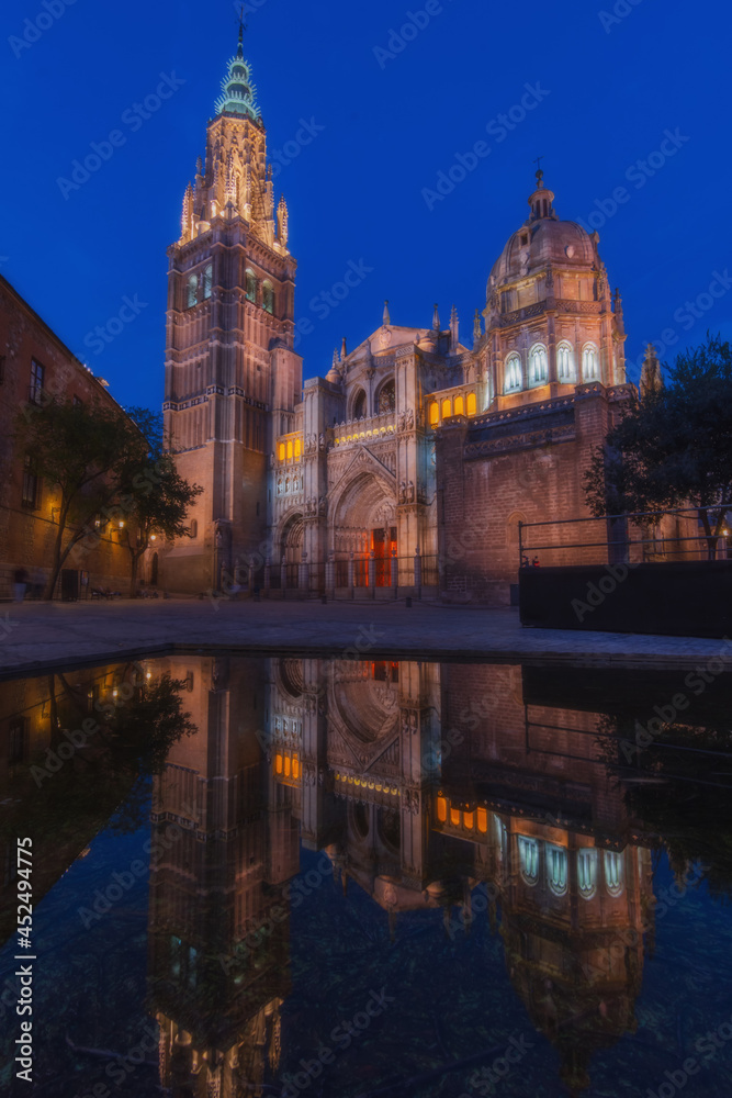 Cityscape in old city night light change; Toledo old town cathedral square with reflection in the water of the fountain - artificial lake, world heritage site, Spain. Vertical view