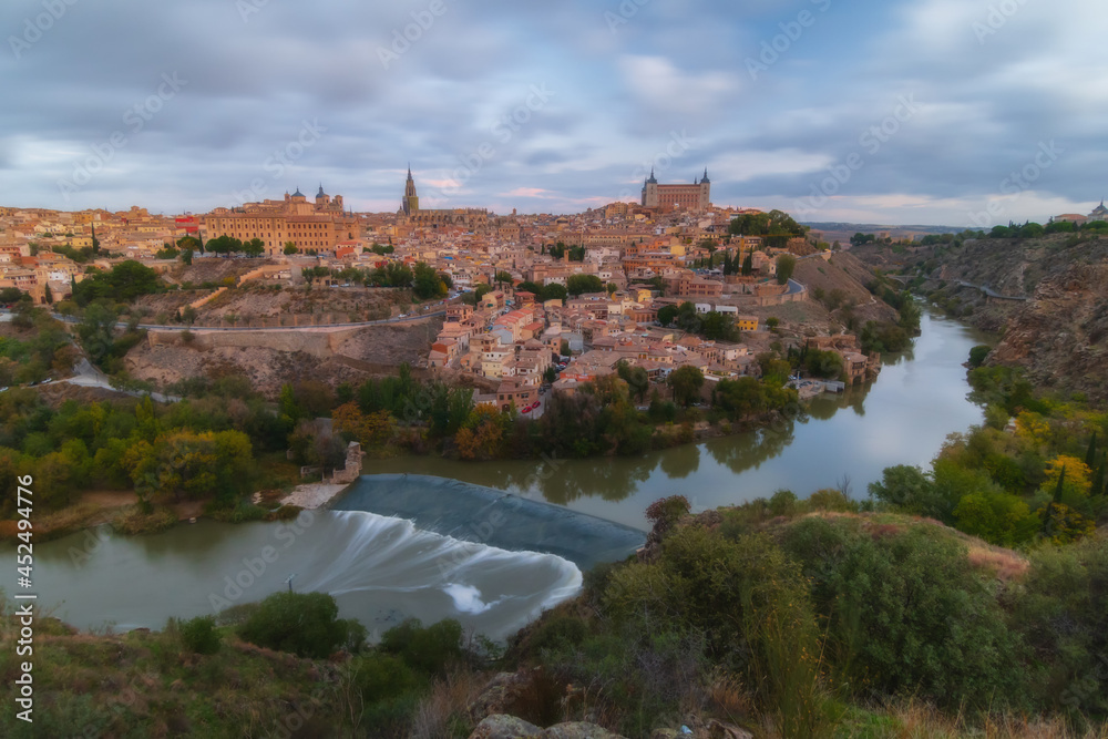 Cityscape in old town with colorful clouds at sunset; Tagus river and old town of Toledo, World Heritage Site, Spain. Horizontal view
