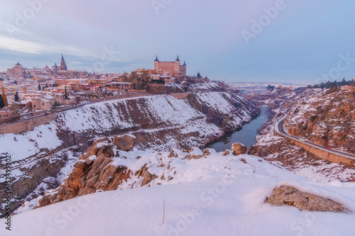 Sunset landscape of snowy old city with colorful clouds and snow; Cathedral and Alcazar of Toledo in temporary Filomena, World Heritage Site, Spain. Horizontal view photo