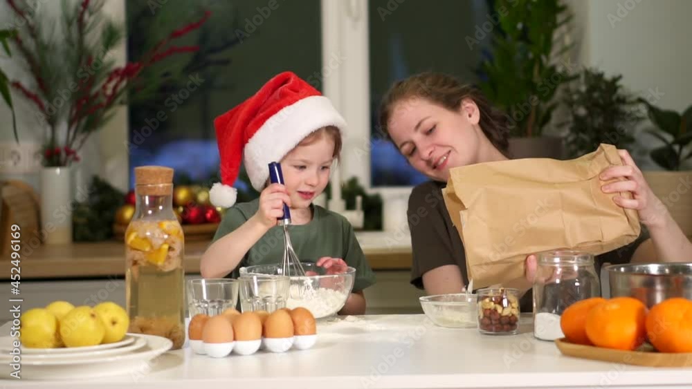 Cook on Christmas Eve. Mom, daughter preparing breakfast New Year holiday. Weekend breakfast in kitchen at table. teaches do child dough flour and eggs. happy family. woman is smiling. girl is play. Cook on Christmas Eve. Mom, daughter preparing breakfast New Year holiday. Weekend breakfast in kitchen at table. teaches do child dough flour and eggs. happy family. woman is smiling. girl is play.