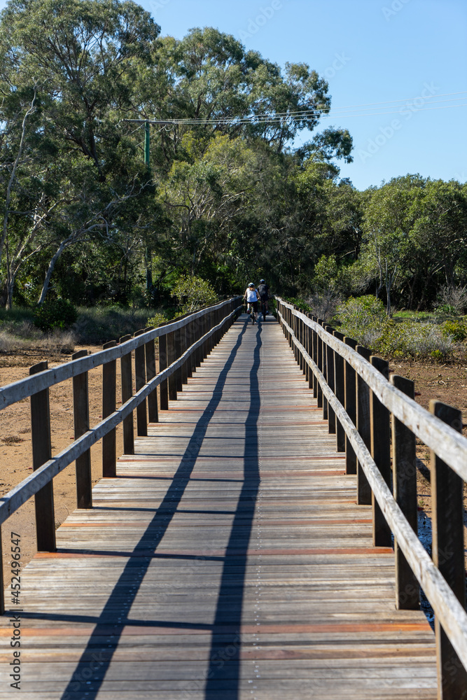 Two people cycling on a boardwalk over the mudflats at Lota, Queensland, Australia.