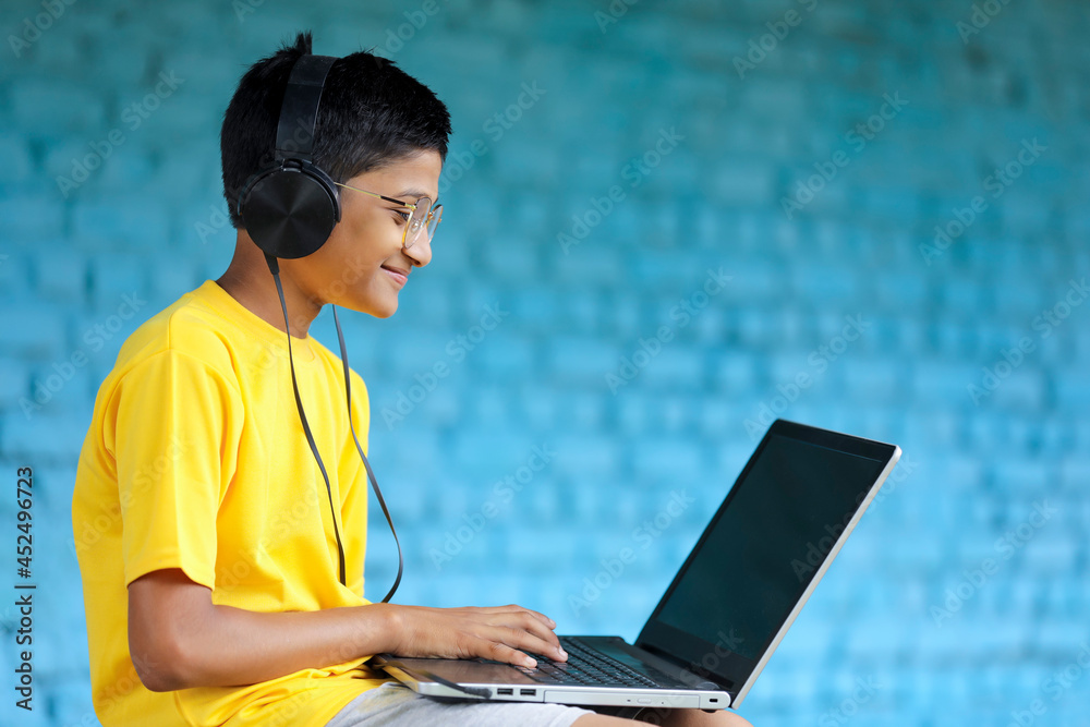 Indian child using laptop and headphone. attending online classes Indian child using laptop and headphone. attending online classes