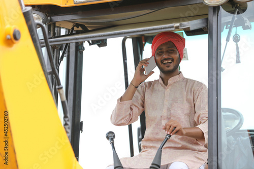 Indian man talking on smartphone and working on heavy earth moving machinery
