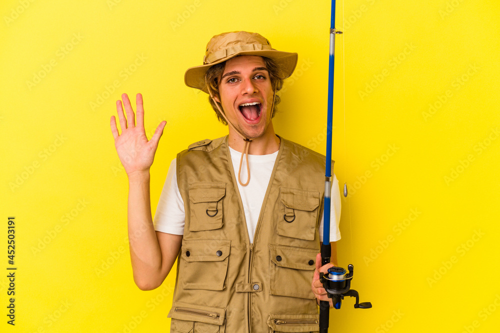 Young fisherman with makeup holding rod isolated on yellow background smiling cheerful showing number five with fingers. Young fisherman with makeup holding rod isolated on yellow background smiling cheerful showing number five with fingers.