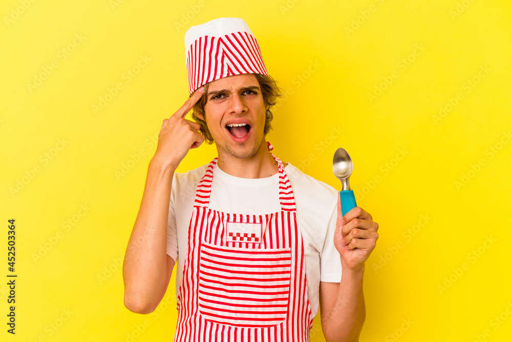 Young ice cream maker man with makeup holding spoon isolated on yellow background  showing a disappointment gesture with forefinger.