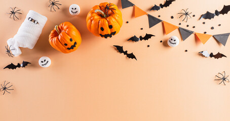 Halloween decorations made from pumpkin, paper bats and black spider on pastel orange background. Flat lay, top view with copy space for text.