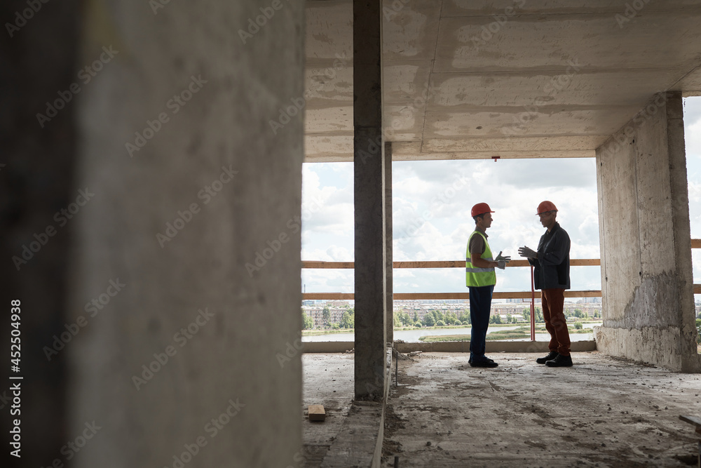 Wide angle view at two workers discussing engineering at costruction site, copy space