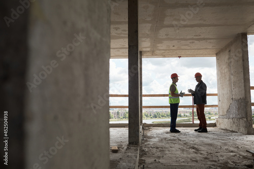 Wide angle view at two workers discussing engineering at costruction site, copy space