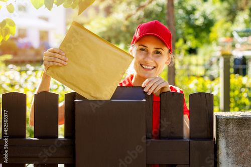 smiling postman mail carrier inserting envelope into mailbox photo