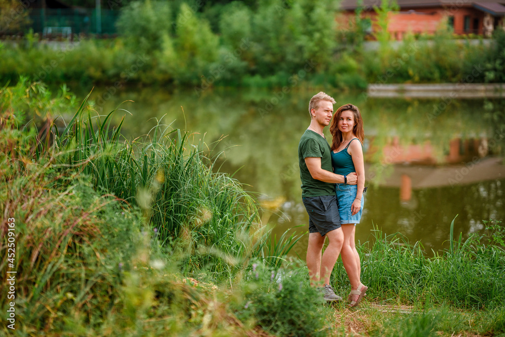 A beautiful couple in love, a man and a woman, embrace on the shore of a summer lake. Amazing natural landscape