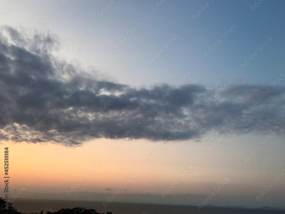 Fototapeta premium Blue and orange sunset sky with sun rays, dark clouds.