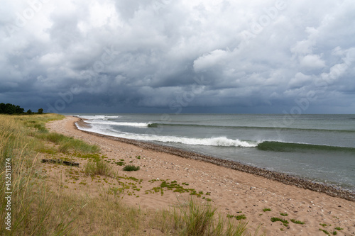 neat waves breaking on a sandy beach with marsh grass and sand dunes and a dark ominous sky overhead