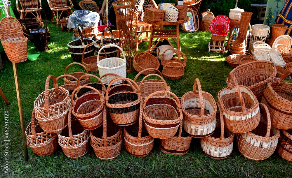 Fototapeta premium A small collection of wicker backets made by hand and used to carry various items seen on a pavement next to a massive shrub during a medieval fair on a Polish countryside