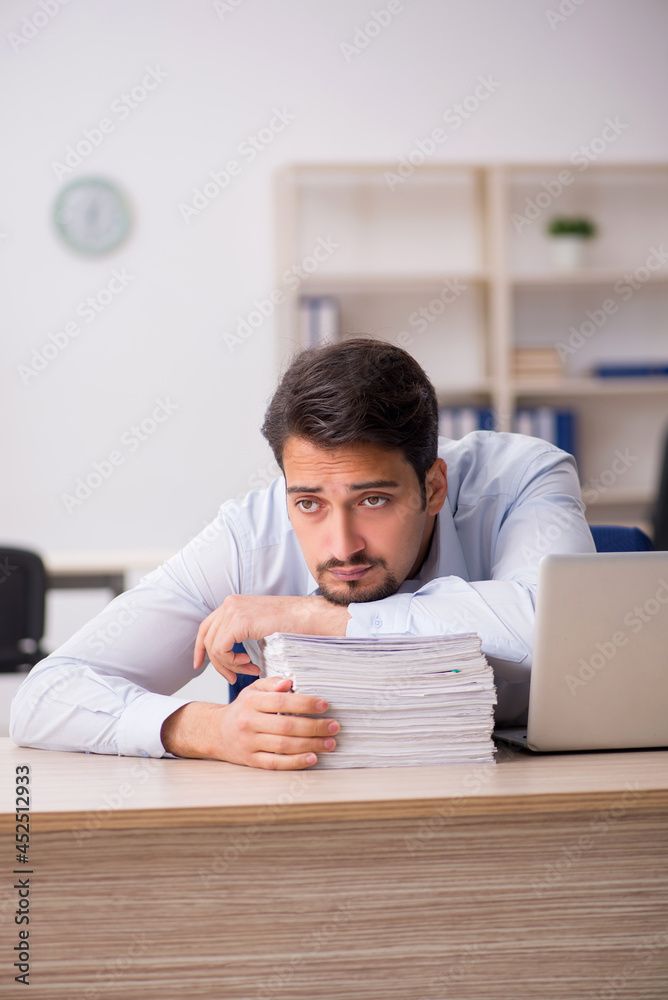 Young male employee unhappy with excessive work in the office Young male employee unhappy with excessive work in the office